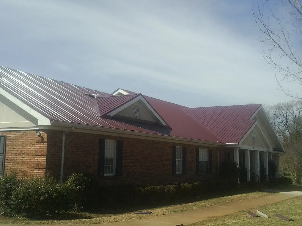 Red metal roof with gabled entries on a long brick building, from a Hail Damage Roof Repair job in Red Oak