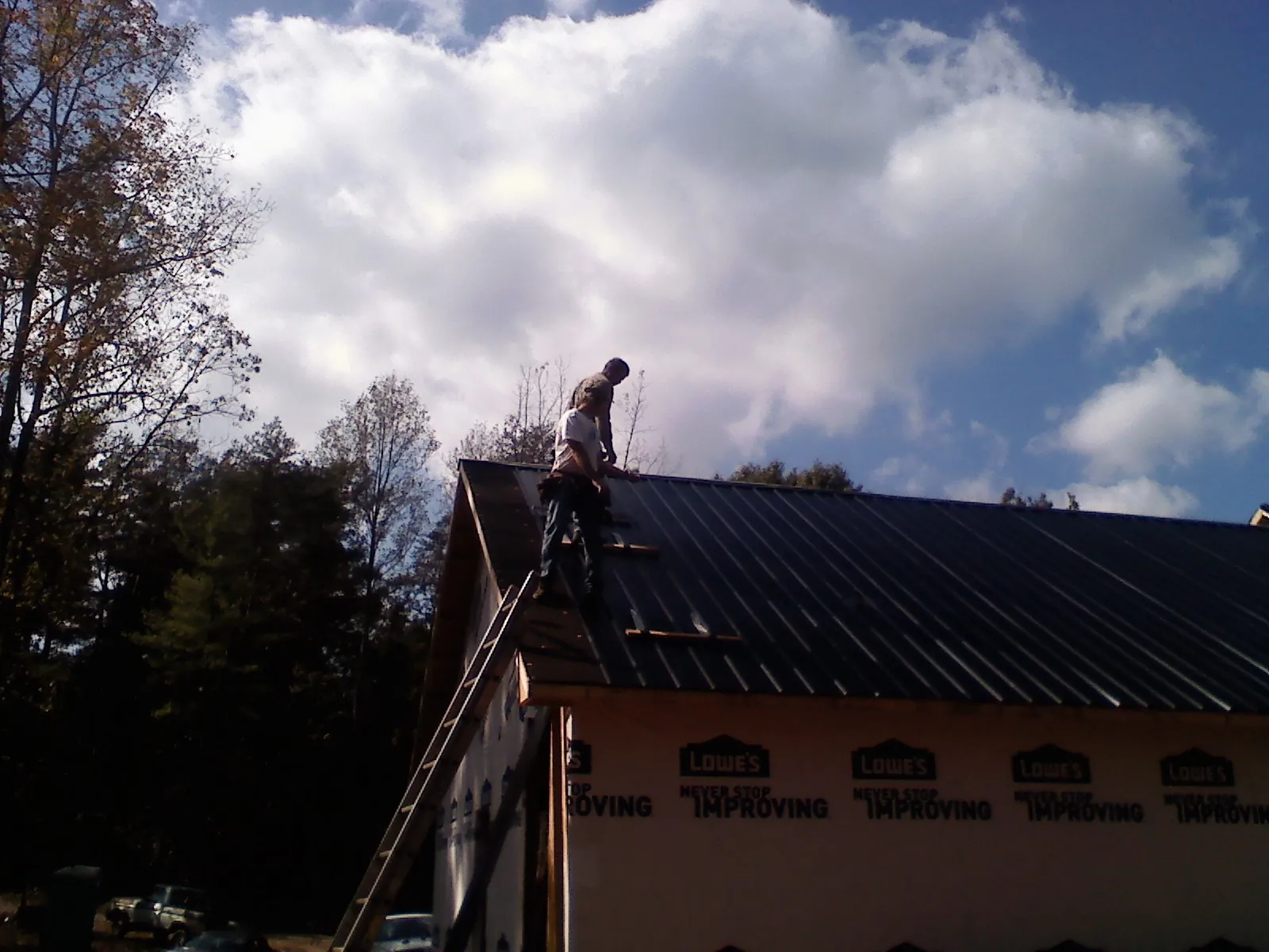 Roofer fastening dark metal panels high against a cloudy sky, from a Roof Inspection job in Red Oak