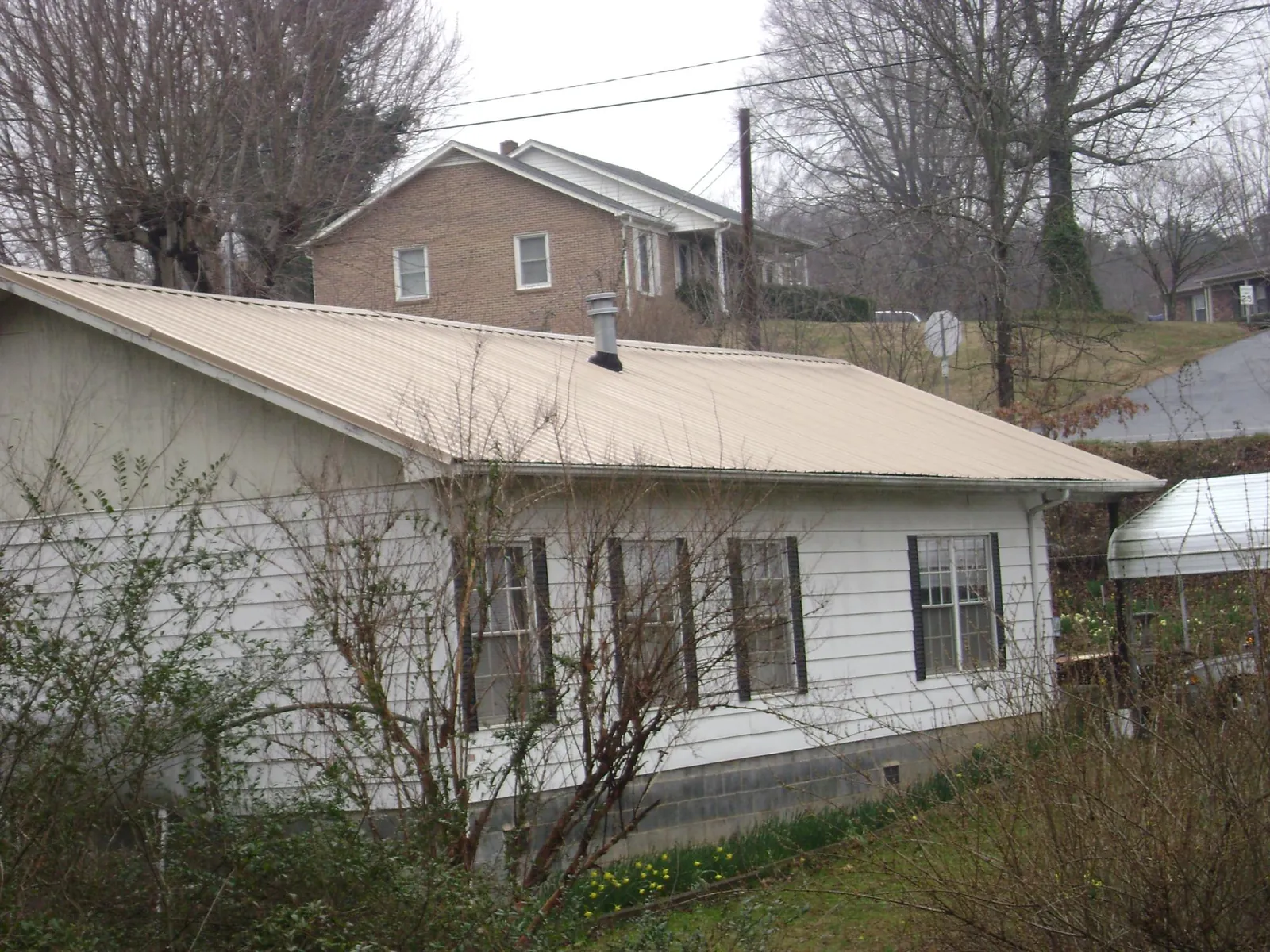 Tan metal roof on a white sided house set into a hillside — Commercial Roofing by Roofing Brothers in Red Oak